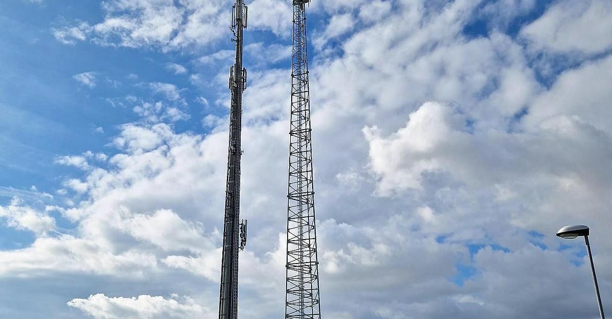 Zwei hohe Telekommunikationstürme stehen gegen einen teilweise bewölkten blauen Himmel. Der Turm auf der linken Seite hat mehrere Antennen, während der auf der rechten Seite eine Gitterstruktur hat.