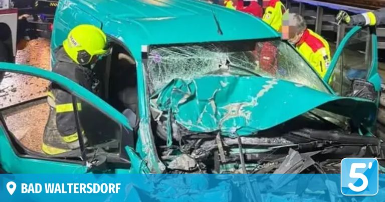 Ein blaues Auto mit zertrümmerter Front, Rettungskräfte in gelben und roten Uniformen sind am Unfallort.