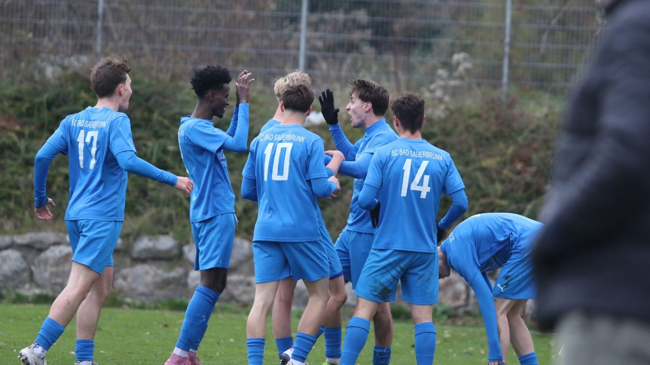 Eine Gruppe von Fußballspielern in blauen Trikots feiert auf dem Feld, ein Spieler trägt Handschuhe.