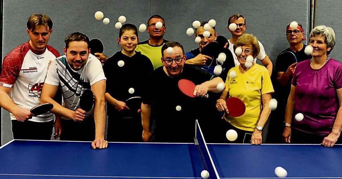 Eine Gruppe von Menschen steht um einen Tischtennistisch herum, hält Schläger und wirft Tischtennisbälle in die Luft. Der Tisch ist blau, und einige Bälle sind noch in der Luft.