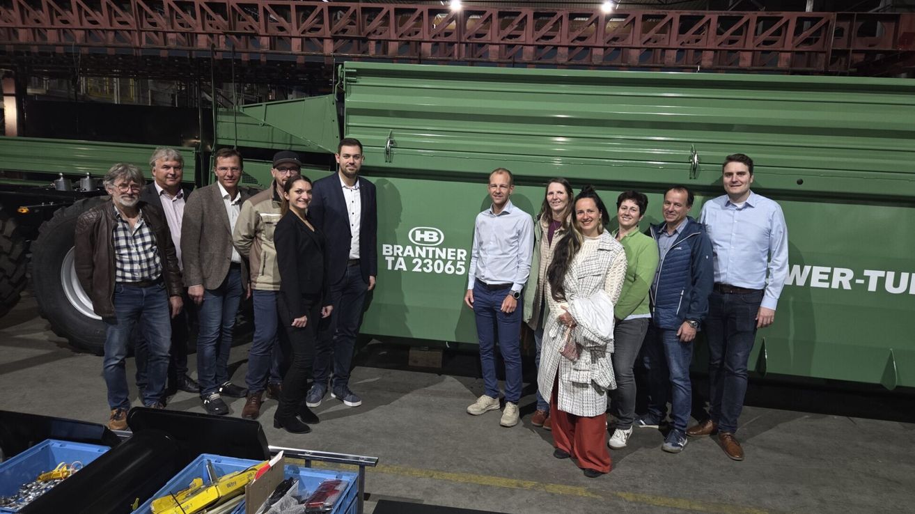 A group of people pose for a picture in front of a green Brantner container. They wear various winter clothing.