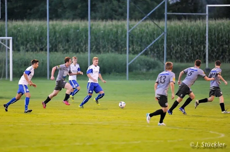 A soccer game is in progress on a well-maintained field. Five players are actively engaged, two wearing white uniforms and three in gray. One player is about to kick the ball.