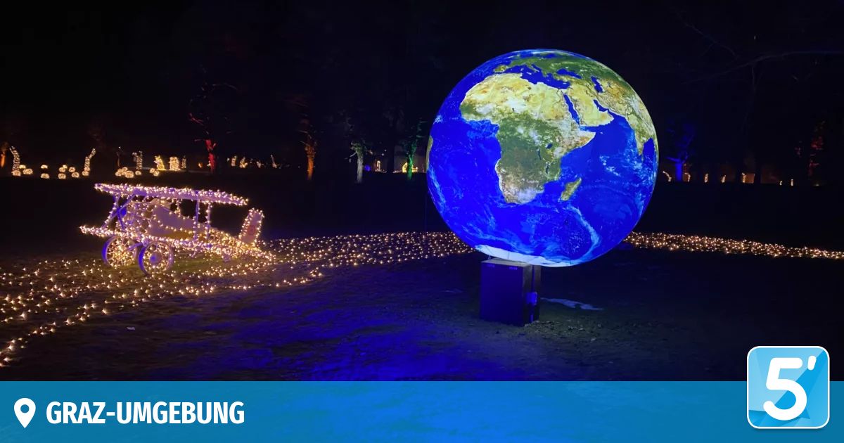 A large illuminated globe is displayed at night, with a trail of lights and a sleigh nearby. Trees and distant buildings are visible.