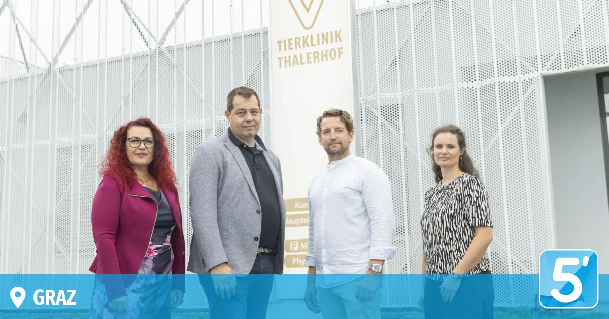 Four people stand in front of a white wall with the words 'Tierklinik Thalerhof'. Three men and a woman smile for the camera. Behind them, a sign indicates a veterinary clinic.