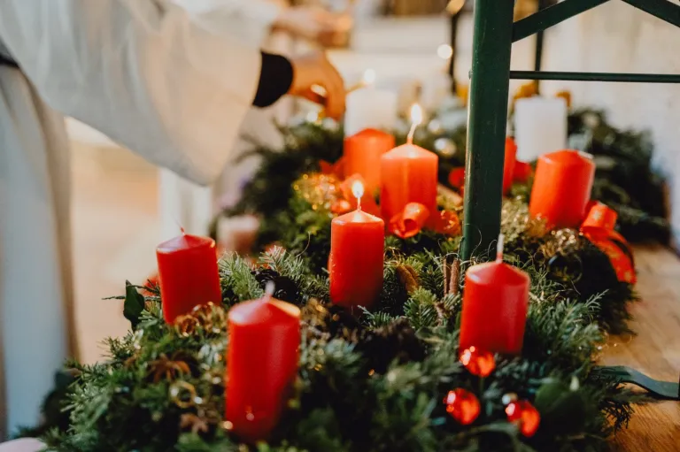 A person is lighting candles on a Christmas wreath with red candles and greenery.