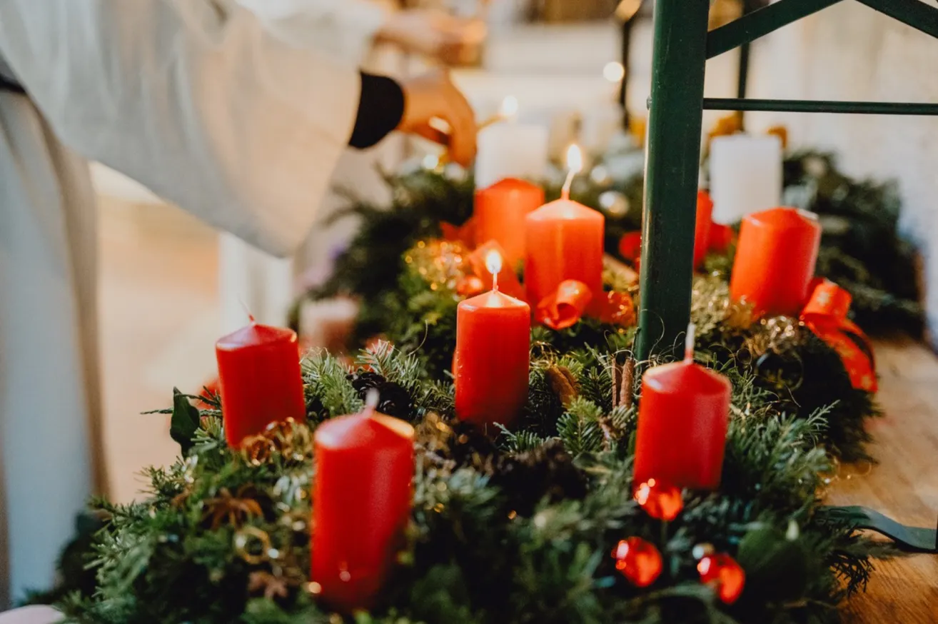 A person is lighting candles on a Christmas wreath with red candles and greenery.