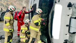 Firefighters are working on a vehicle accident with one person inside. The vehicle is tilted on its side. The firefighters are wearing protective gear.