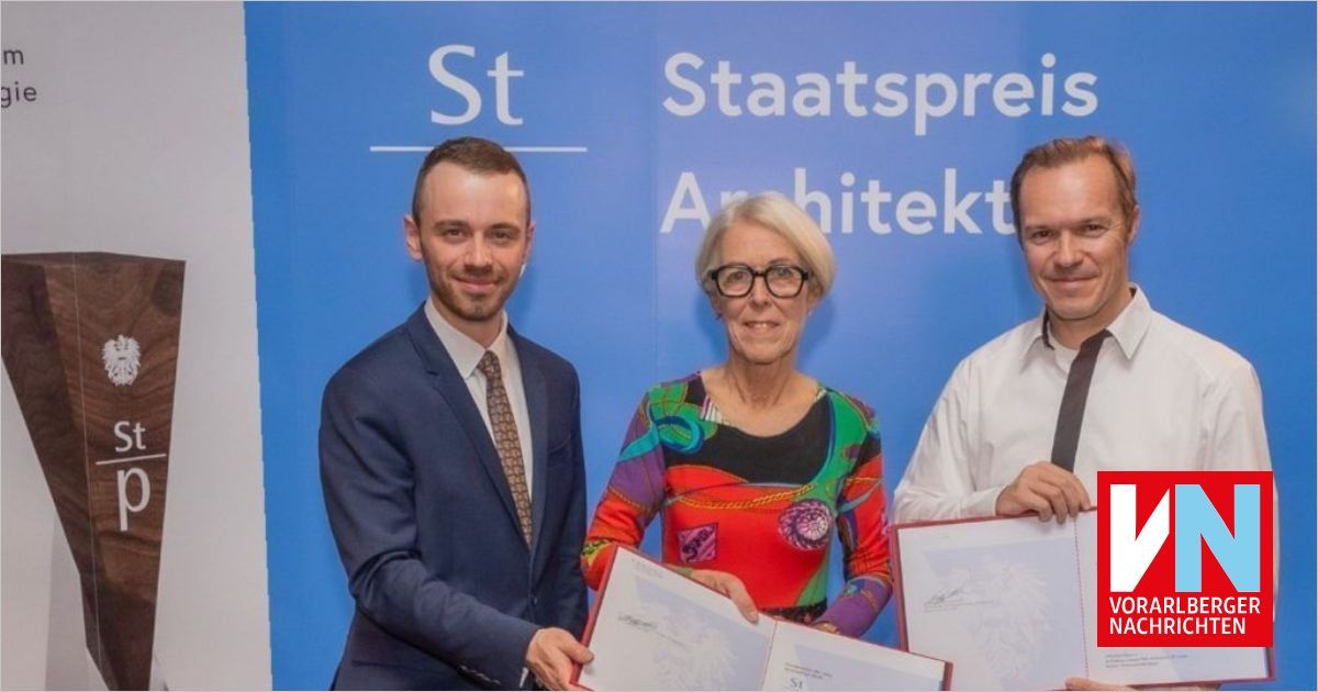 Three individuals stand together holding certificates. The man on the left wears a suit and tie, while the woman in the middle holds a framed certificate. The man on the right also holds a framed certificate. They stand in front of a blue banner with white text.