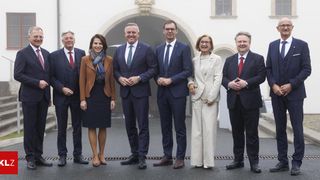 A group of formally dressed individuals stands outside a historic building with an arched entrance. They are smiling and appear to be posing for a photograph.