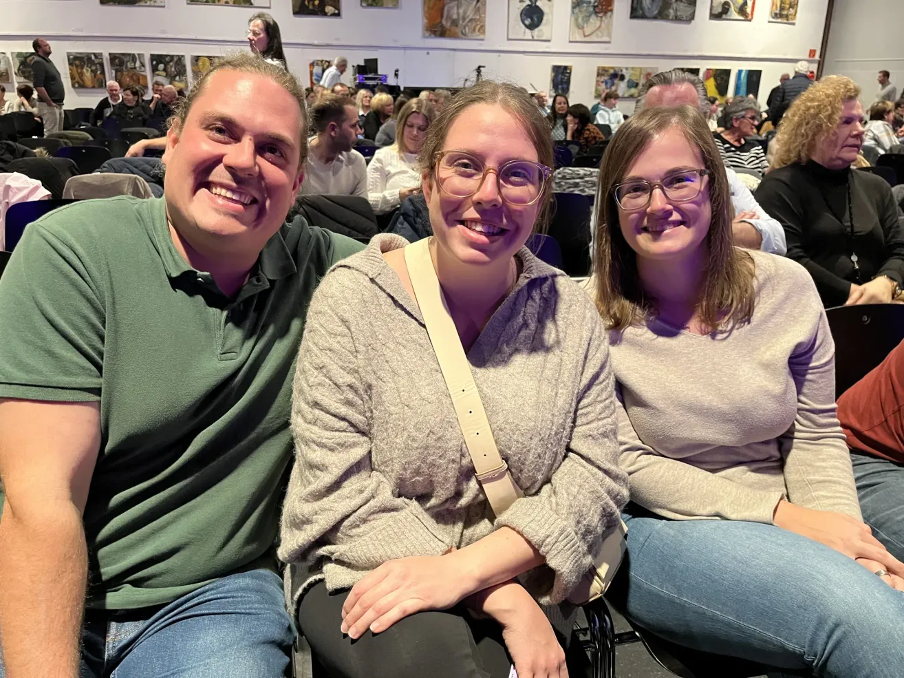 Three people sit together in a room with smiling faces, two women and a man. They appear to be posing for a photo.