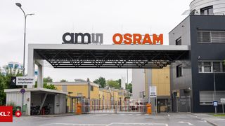 An entrance to the Osram facility displays the company logo. The building is yellow, and bicycles are parked outside. The road is empty.