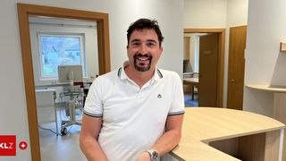 A man wearing a white polo shirt stands in a hospital room, smiling for a photo.