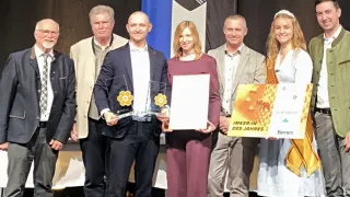 A group of people, possibly winners, are standing on a stage holding awards and certificates. They are smiling and posing for a photo.
