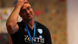 A man wearing glasses and a black shirt with the word 'Xentis' on it. He is holding his head with his left hand.