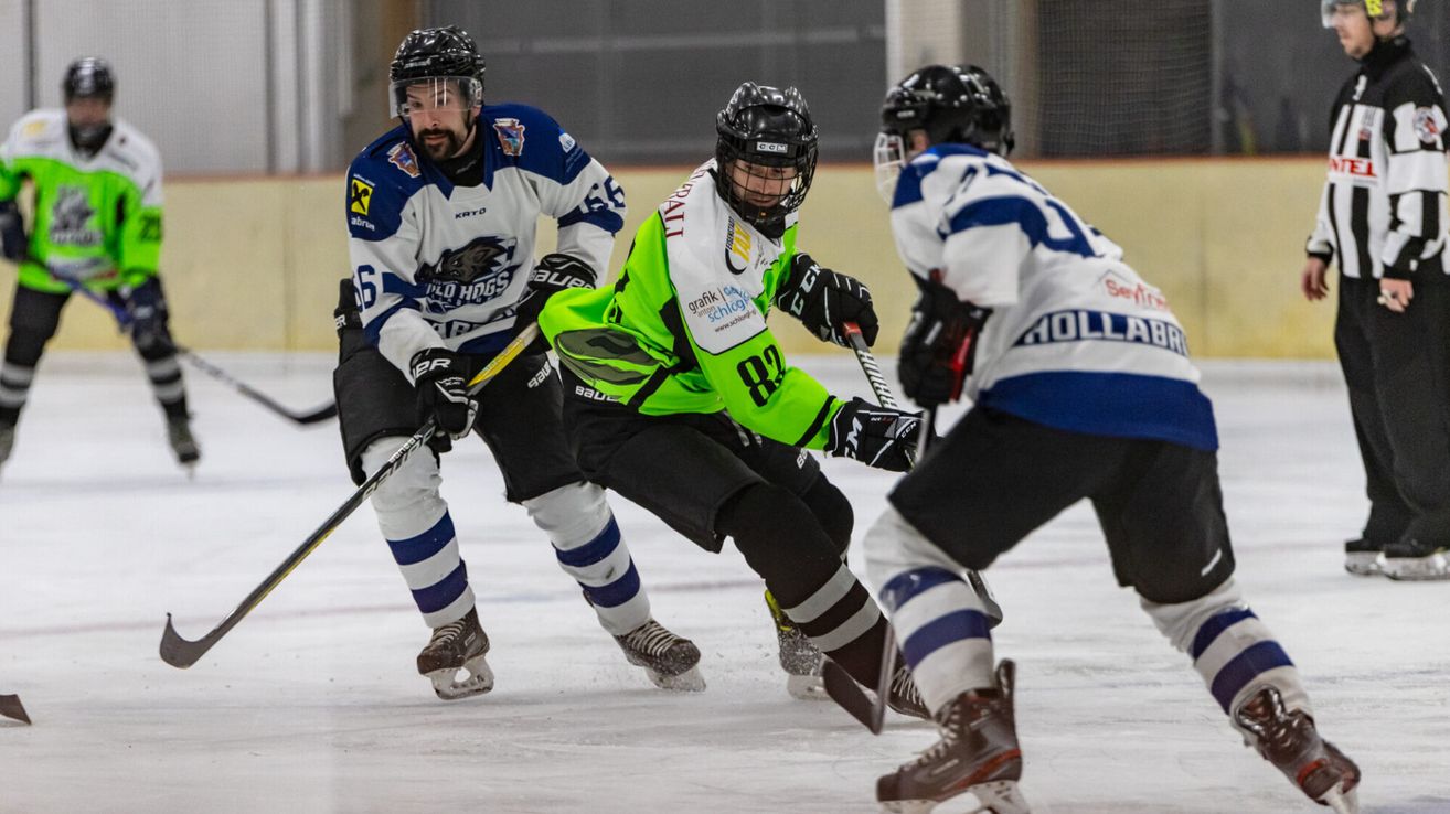 Three hockey players are on an ice rink. The player in green skates forward while two others try to block him. All wear helmets, gloves, and hockey skates.