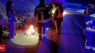 Emergency responders gather around a fire at night on a road, one holding a paper and another with a reflective vest.