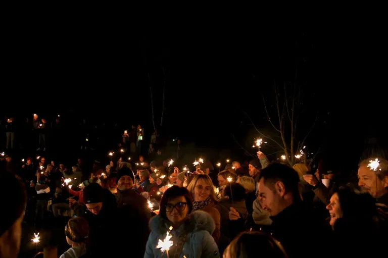 Eine Menschenmenge bei Nacht hält Wunderkerzen, schaut nach oben und lächelt, erleuchtet von ihren Lichtern.