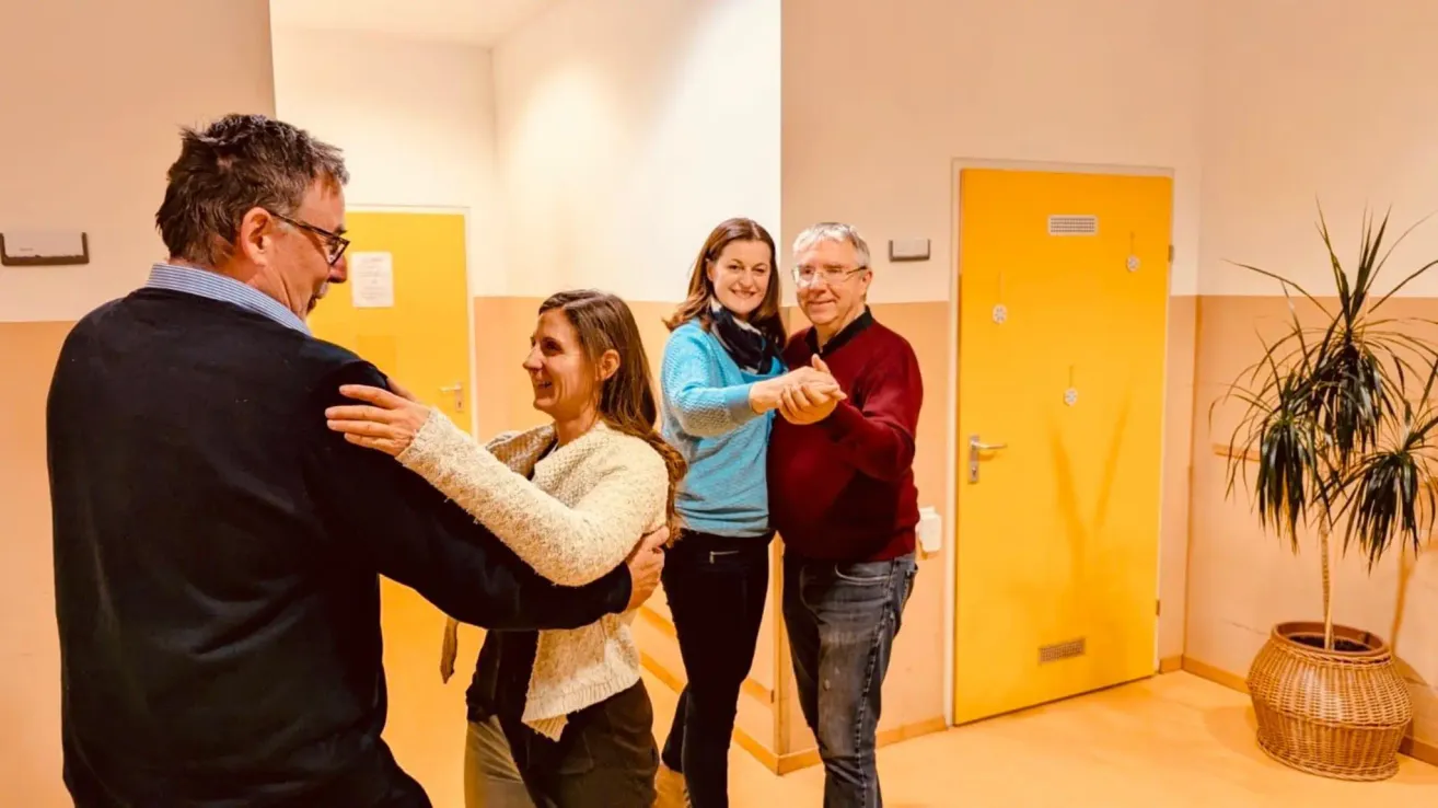 Four people are dancing in a room with yellow walls and doors. The two women and two men are smiling and appear to be enjoying themselves.