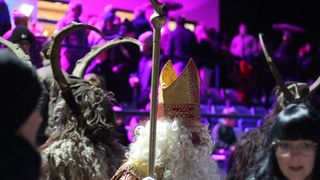 A person in a bishop's mitre and robe stands in front of a crowd with purple lighting in the background.