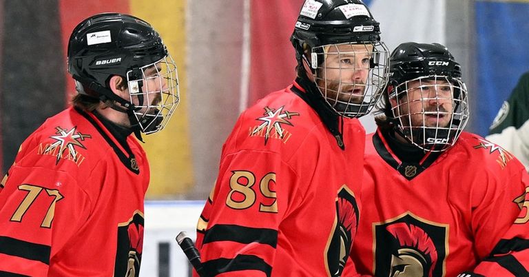 Three hockey players in red jerseys and helmets stand on an ice rink. One player wears the number 89.