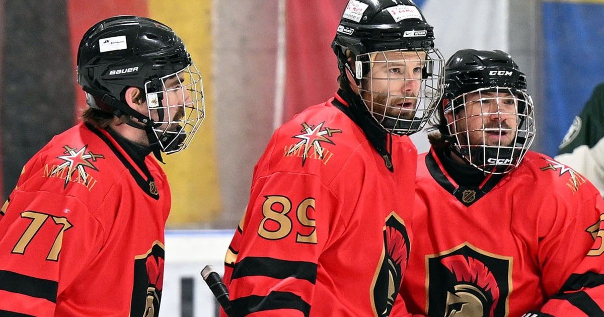 Three hockey players in red jerseys and helmets stand on an ice rink. One player wears the number 89.