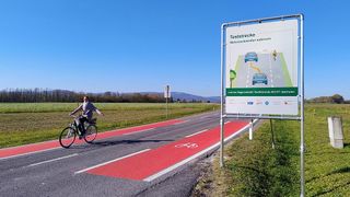 A cyclist rides on a red cycle lane on a rural road with a sign indicating test lanes for cyclists.
