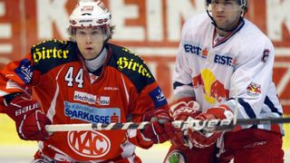Two hockey players on an ice rink, one holding a hockey stick. Player 44 wears a red and black jersey with 'electronic4you' and 'De Kärntner Sparkasse'. The other player wears a red and white jersey with 'BAUER' and 'EIST'. Both are in red gloves.