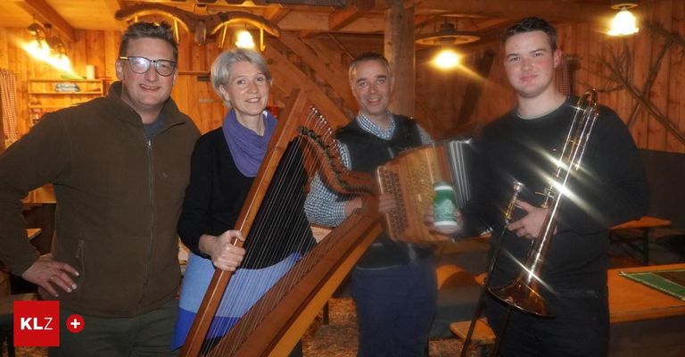 Vier Personen stehen zusammen in einer Scheune. Eine Frau hält eine Harfe und ein Mann neben ihr ein Akkordeon. Ein weiterer Mann hält eine Posaune und ein vierter Mann steht links.