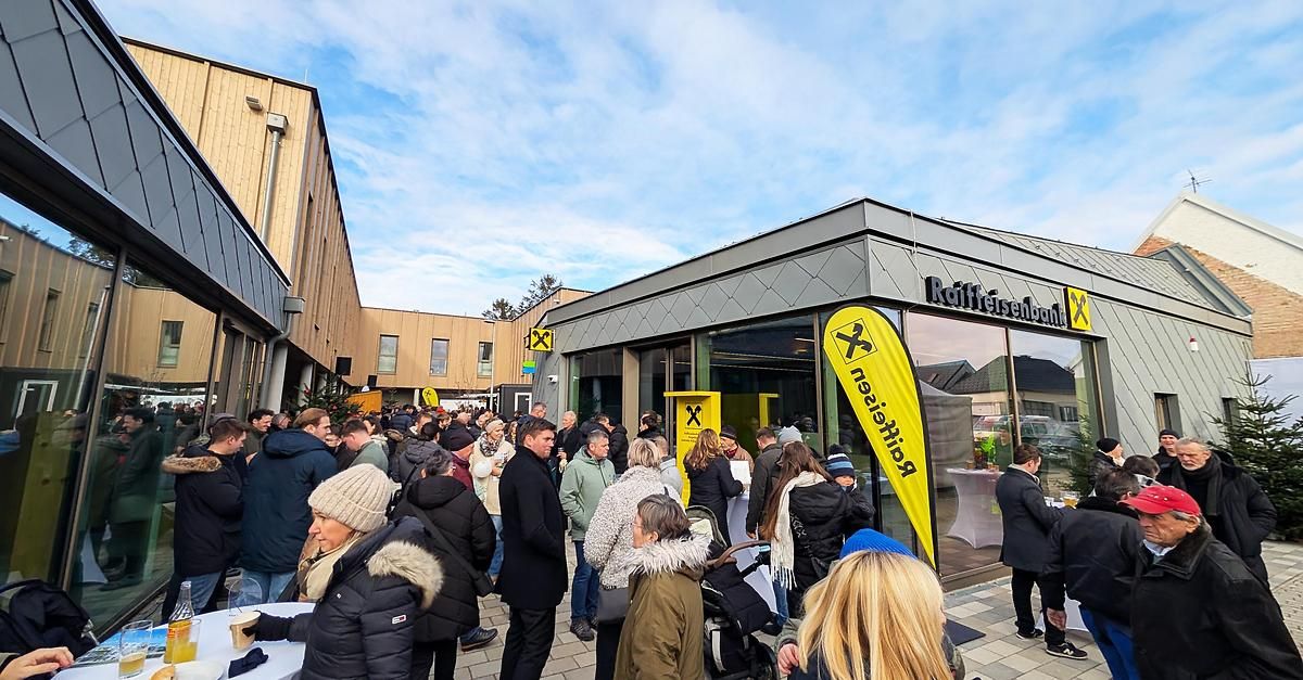 Eine Menschenmenge versammelt sich vor einem Gebäude, möglicherweise in einer Warteschlange. Es gibt zwei gelbe Banner mit dem Wort 'Premium'. Ein Gebäude mit Glasfenstern und einem Schild, das 'Raffleseisenbahn' besagt, ist sichtbar. Vor dem Gebäude sind Autos geparkt.