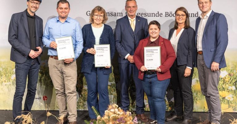 Fünf Personen stehen zusammen, lächeln und halten Urkunden in den Händen. Der Hintergrund trägt die Aufschrift 'Zusammen für gesunde Bodensee'. Die Frau in der Mitte trägt einen roten Blazer, während die anderen blaue und weiße Hemden tragen.