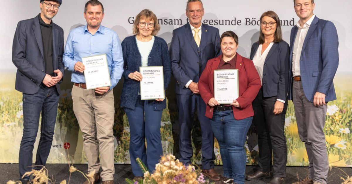 Fünf Personen stehen zusammen, lächeln und halten Urkunden in den Händen. Der Hintergrund trägt die Aufschrift 'Zusammen für gesunde Bodensee'. Die Frau in der Mitte trägt einen roten Blazer, während die anderen blaue und weiße Hemden tragen.