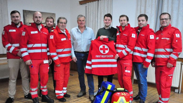 Eine Gruppe von Personen in roten Ersthelferuniformen posiert für ein Foto mit einem Mann in einem hellblauen Hemd.