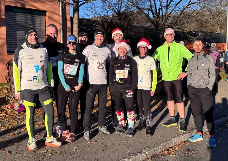 Eine Gruppe von Menschen, die Winterkleidung und Weihnachtsmützen tragen und Nummern auf ihren Trikots haben, posiert für ein Foto auf einer Straße.