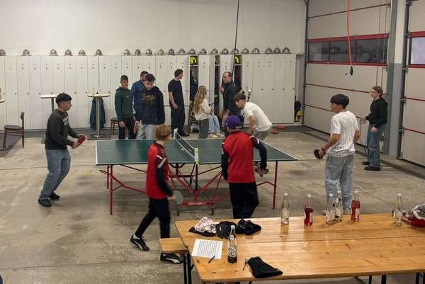 Eine Gruppe von Menschen spielt Tischtennis in einem Raum mit Schließfächern und einem Tisch.