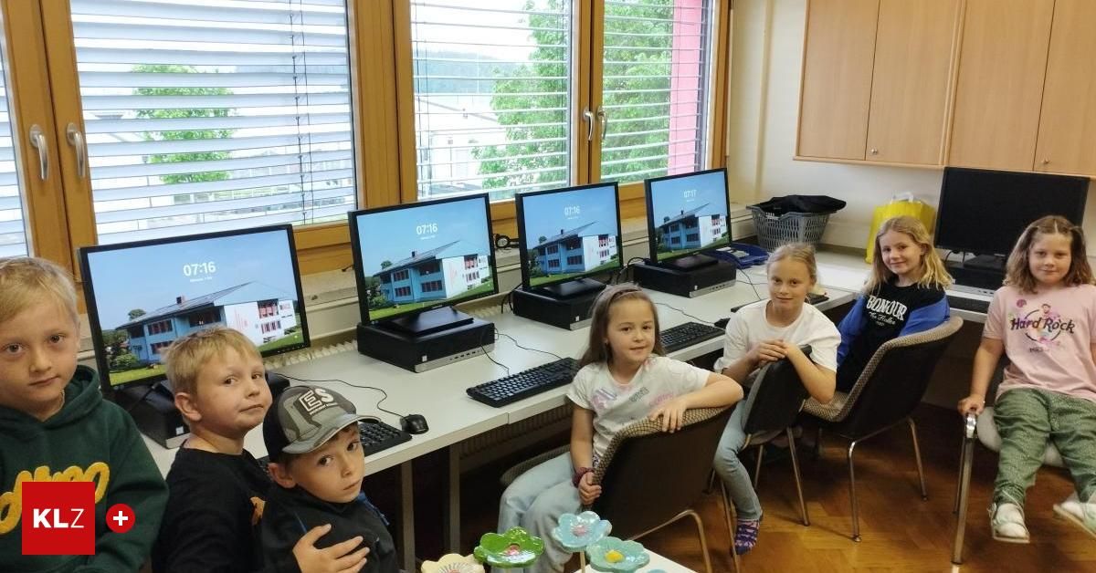 Fünf Kinder sitzen an einem Computerschreibtisch mit Monitoren, die ein Gebäude zeigen. Sie lächeln und scheinen ihre Zeit zu genießen.