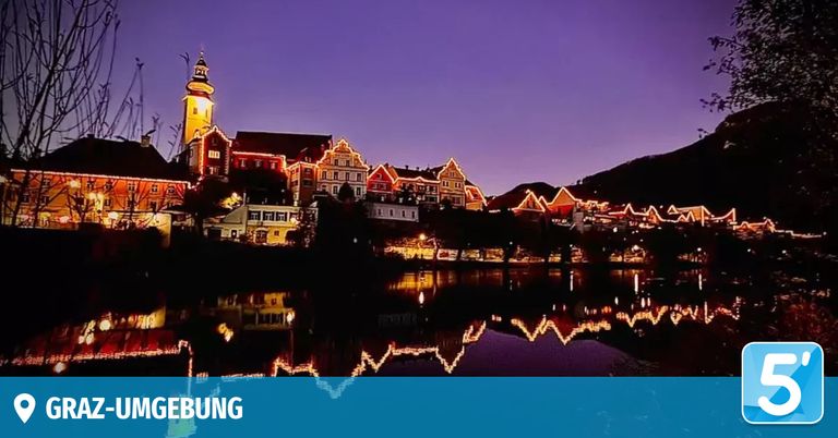 Eine malerische Stadt in der Dämmerung mit beleuchteten Gebäuden, einem Turm und Reflexionen auf einem Fluss.