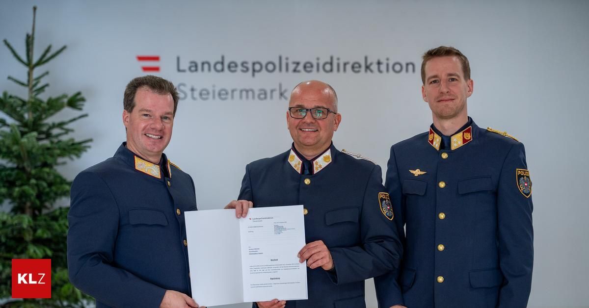 Drei Männer in Uniform stehen zusammen und halten ein Zertifikat. Der Mann in der Mitte trägt eine Brille. Hinter ihnen steht ein Schild mit der Aufschrift 'Landespolizeidirektion Steiermark'.