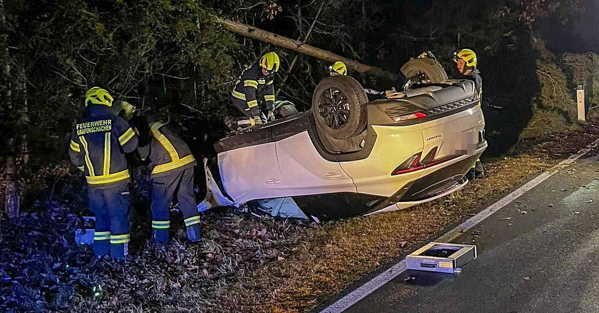 Feuerwehrleute kümmern sich um ein umgestürztes Auto am Straßenrand. Das Auto liegt auf der Seite, und die Feuerwehrleute bereiten sich darauf vor, die Insassen zu retten.