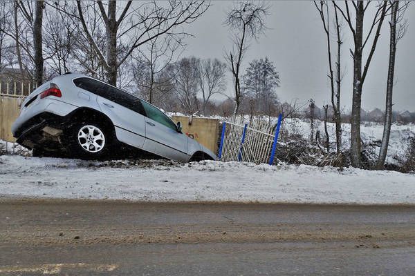 Ein silberner SUV ist auf schneebedecktem Boden seitlich geneigt, wobei sich ein Rad in der Luft befindet. Bäume umgeben das Fahrzeug.