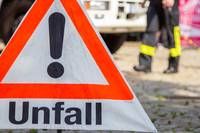 Ein dreieckiges Schild mit orangefarbenen und weißen Farben, das eine Unfallwarnung anzeigt. Das Wort 'Unfall' ist in fetten schwarzen Buchstaben geschrieben. Im Hintergrund ist eine Person in reflektierenden Kleidungsstücken zu sehen.