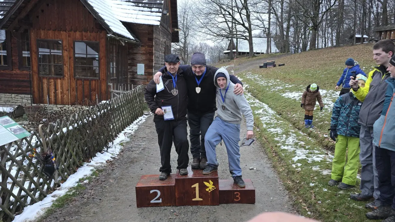 Drei Personen stehen auf einem Podest, zwei Männer mit Medaillen um den Hals und ein Junge, der ein Papier in der Hand hält. Sie befinden sich in einem verschneiten Bereich.