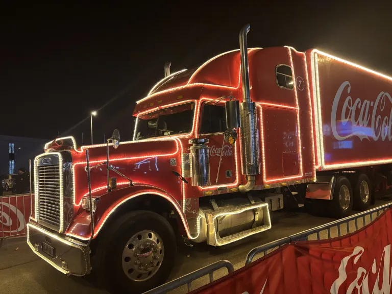 Ein roter Coca-Cola-Lkw ist mit roten Lichtern dekoriert und nachts auf einem Parkplatz geparkt.