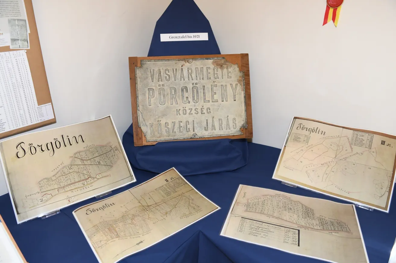 Eine Ausstellung auf einem Tisch umfasst eine alte Karte, ein Schild mit dem Text 'VASVARMEGYE PORCULENY KOZSEC' und andere Dokumente. Das Schild zeigt die Grenze bis 1921 an.