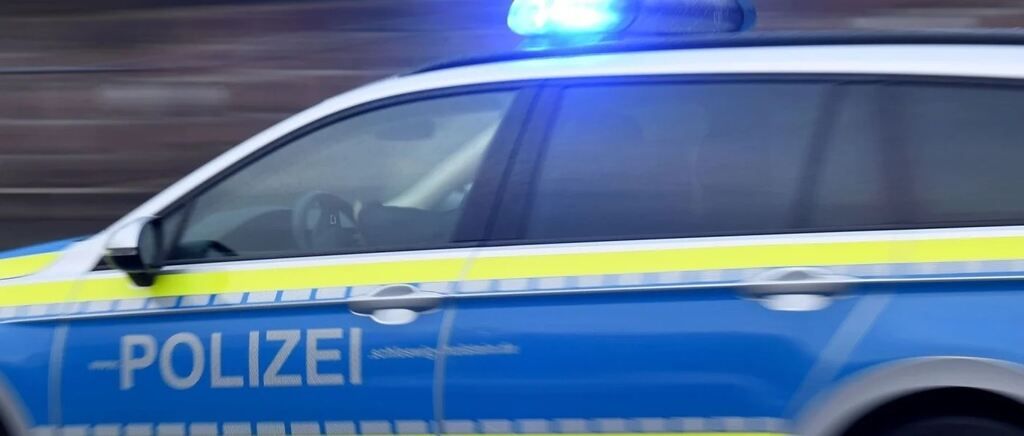 Ein verschwommenes Bild eines Polizeiwagens mit blinkenden Lichtern oben, dem Wort 'POLIZEI' an der Seite und einer verschwommenen Ansicht der Straße bei Nacht.