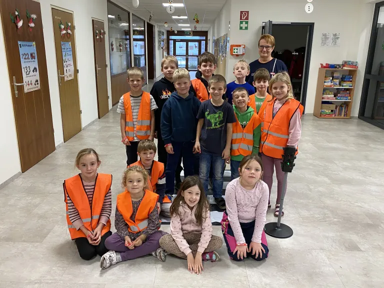 Eine Gruppe von Kindern in Sicherheitswesten posiert für ein Foto in einem Flur.