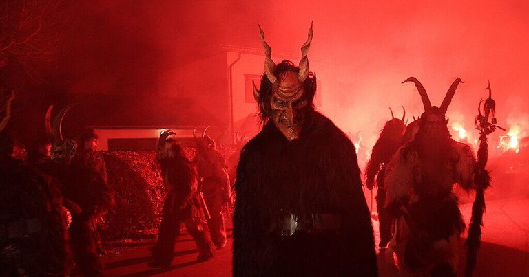 Eine Gruppe von Menschen mit Hörnermasken geht durch einen rot beleuchteten Bereich, möglicherweise für ein Festival.