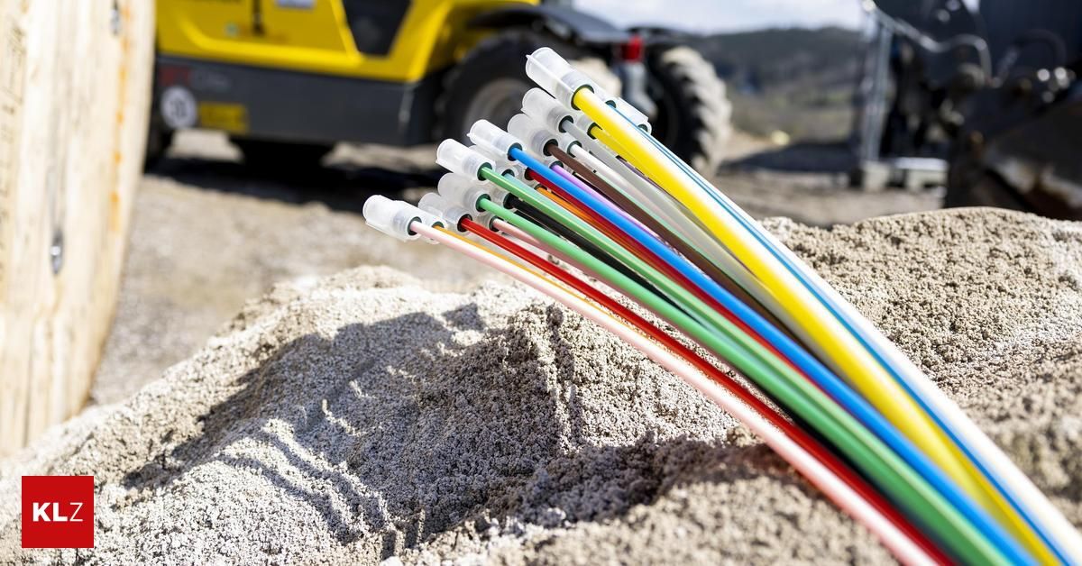 Eine Sammlung mehrfarbiger Drähte liegt auf einem Haufen Sand, mit einem gelben Baufahrzeug im Hintergrund.