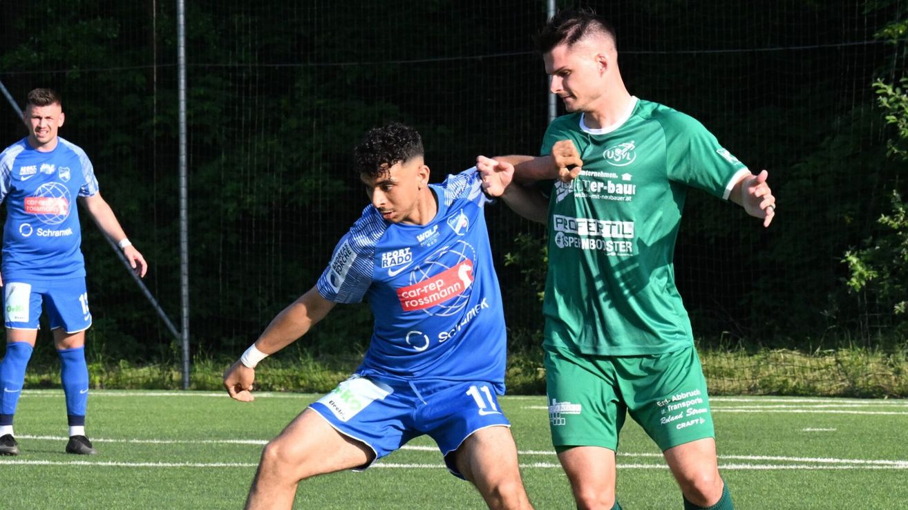 Zwei Fußballspieler auf einem Feld. Einer in Blau, Nummer 11, und einer in Grün. Sie ringen während eines Spiels.