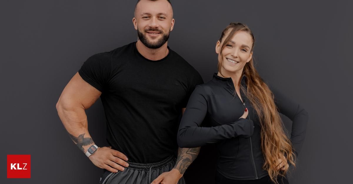 Ein Mann und eine Frau posieren für ein Foto, beide tragen schwarze Trainingskleidung. Der Mann hat ein Tattoo auf seinem linken Arm, und die Frau hat lange Haare.