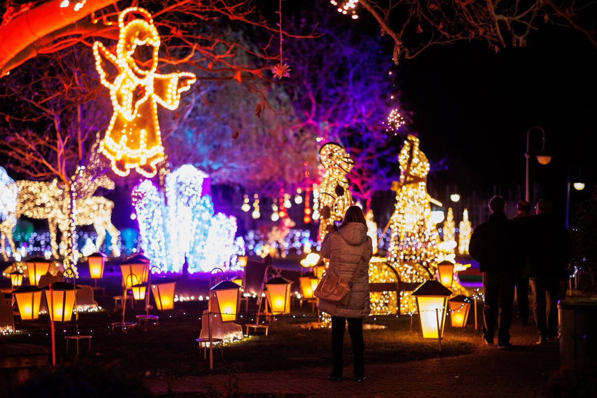 Eine Frau steht nachts in einem Park und bewundert eine Ausstellung illuminierter Dekorationen, darunter Laternen und leuchtende Figuren.